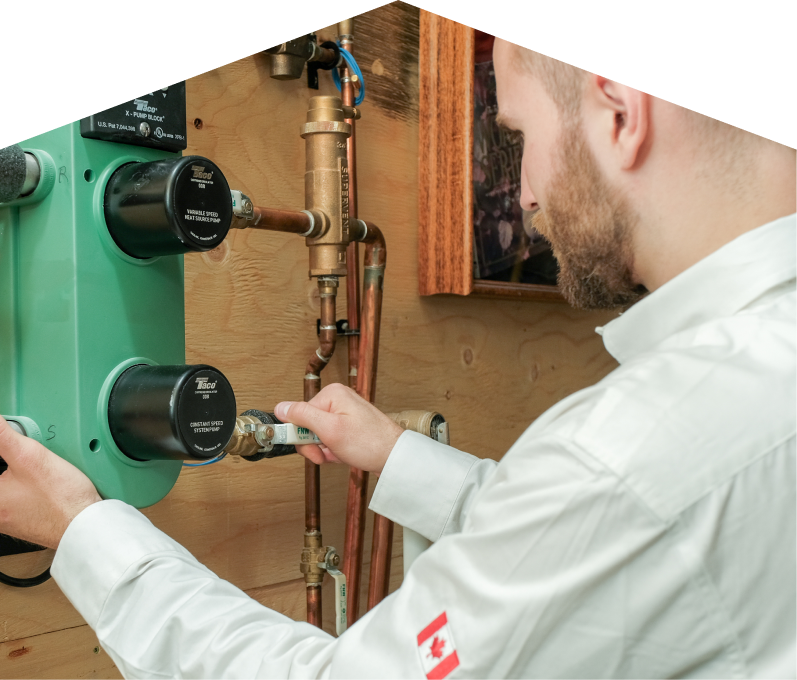 Romaniuk HVAC specialist performing boiler installation, securing a valve on a new hydronic heating system with copper piping and a green circulation pump mounted on a wooden wall. Romaniuk HVAC specialist performing boiler installation, securing a valve on a new hydronic heating system with copper piping and a green circulation pump mounted on a wooden wall.